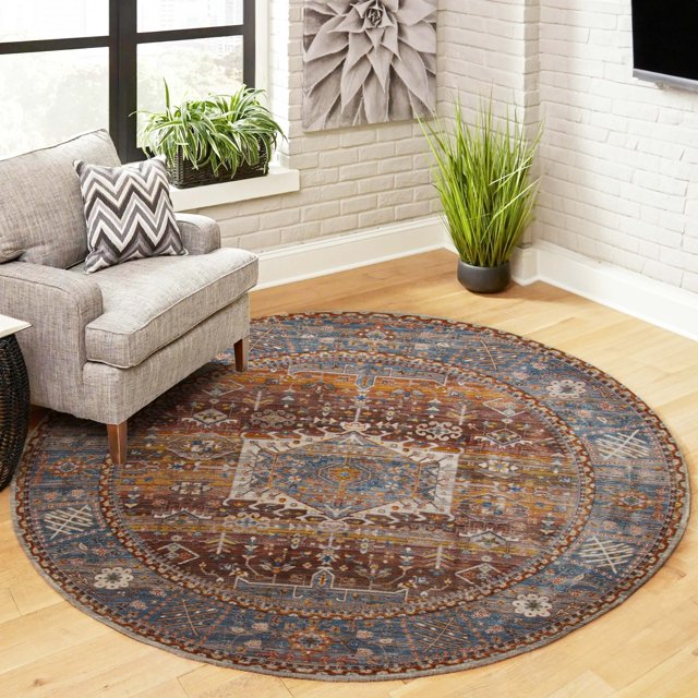 Round ECARPET Dulce traditional area rug featuring intricate blue, brown, and beige designs on a wooden floor next to a gray armchair in a bright living room.