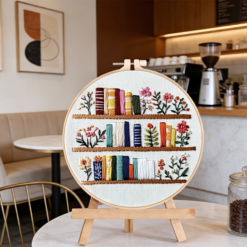 An Embroidery Kit Featuring a Bookshelf Floral Pattern Measuring, Suitable for Both Adults And Beginners. It Includes Instructions, Printed Fabric, an Embroidery Hoop, And Needle And Thread