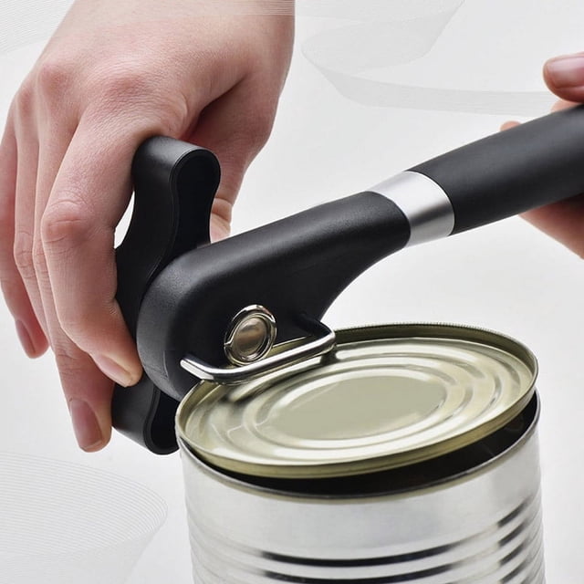 abrelatas manual de borde liso, abrelatas de mano sin bordes afilados con agarres suaves. Vista frontal en uso: abridor negro ergonómico con mango largo y perilla grande giratoria colocado en la tapa de una lata metálica; hoja de corte de acero inoxidable visible en el borde y orificio para colgar en el mango. Tamaño compacto, adecuado para llevar al acampar.