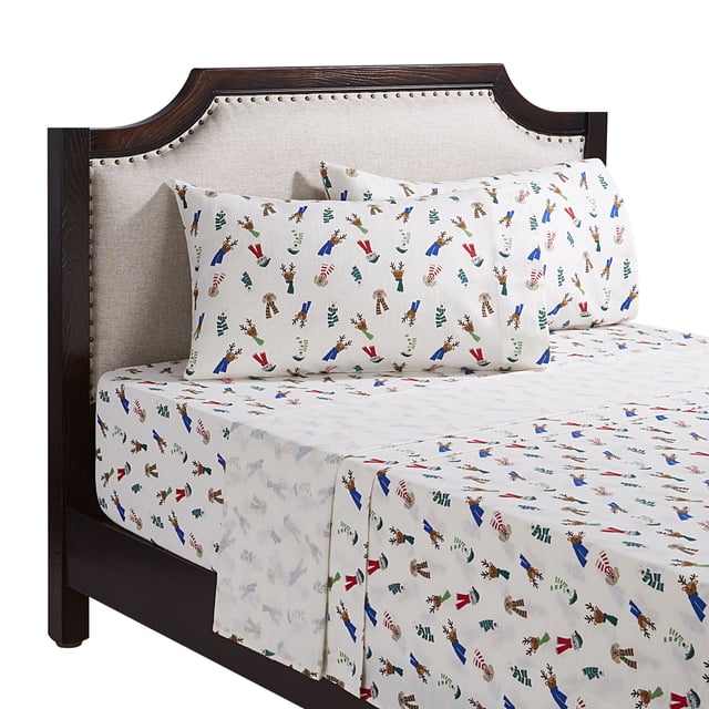 Holiday Time queen flannel sheet set featuring festive reindeer wearing colorful scarves on white background, displayed on bed with dark wood frame and beige upholstered headboard.