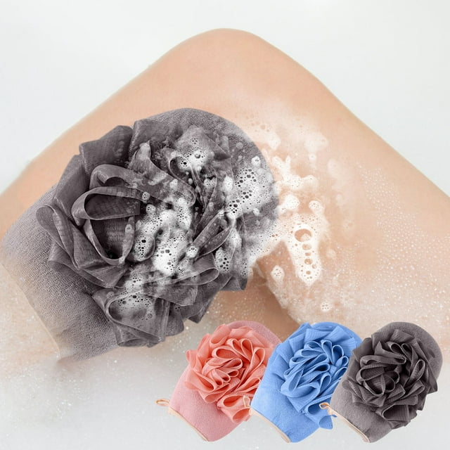 esponja de baño de doble cara con textura de arena fina y lado suave para adultos, estropajo exfoliante para el cuerpo. Vista frontal centrada de la esponja en forma de flor con pliegues rizados y lazo de colgado; en primer plano aparecen las opciones de color rosa, azul y gris sobre fondo claro con espuma. Según especificaciones, diseñada para exfoliación y masaje; a menudo usada también para frotar la espalda.