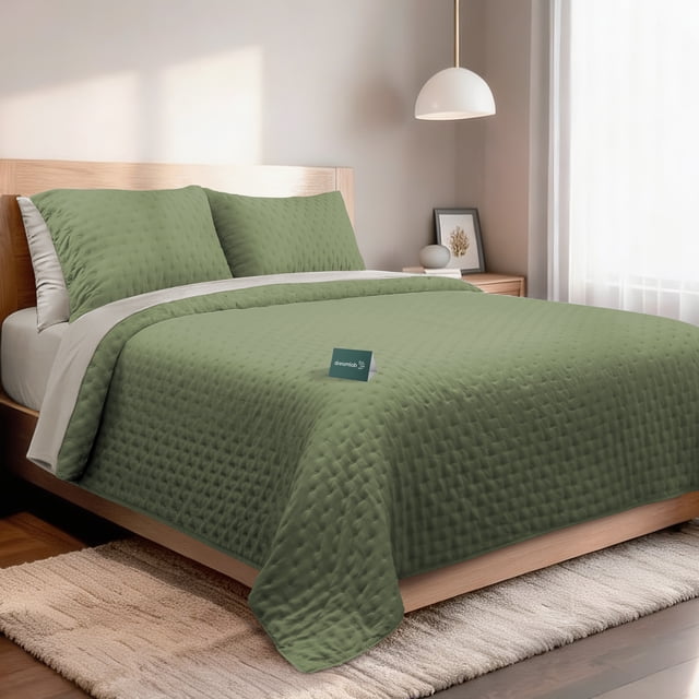 set de 7 piezas edredón ligero y sábanas matrimonial dreamlab, colcha para cualquier temporada, hipoalergénica, diseño trébol verde seco, beige — Cama matrimonial vestida con colcha ligera verde seco acolchada en rombos y reverso beige, dos fundas decorativas verdes sobre almohadas blancas y sábana plana beige visible; tela microfibra doble cepillado, etiqueta Dreamlab en el centro, cabecero de madera y mesita de noche en habitación iluminada. También incluye bajera ajustable apta para colchones altos según talla matrimonial.
