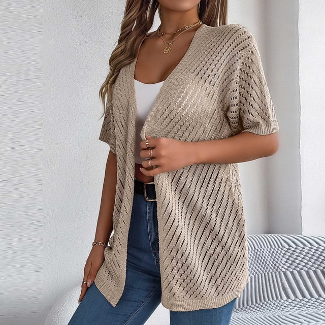 Cardigan de Mode pour Femmes Cameland d'Automne, Couleur beige Unie avec design en Tricot Ajouré et Manches Courtes. le Cardigan Style Ouvert sur un Haut Blanc et Assorti à des jeans Bleus. Fait de 95 % polyester et 5 % Élasthanne, Il Est Léger, Doux et Confortable, Convient pour un Usage Décontracté, Quotidien Ou de Fête. le Modèle Est Accessoirisé avec des Bijoux Dorés et Se Tient Debout dans un Cadre Intérieur Minimaliste.