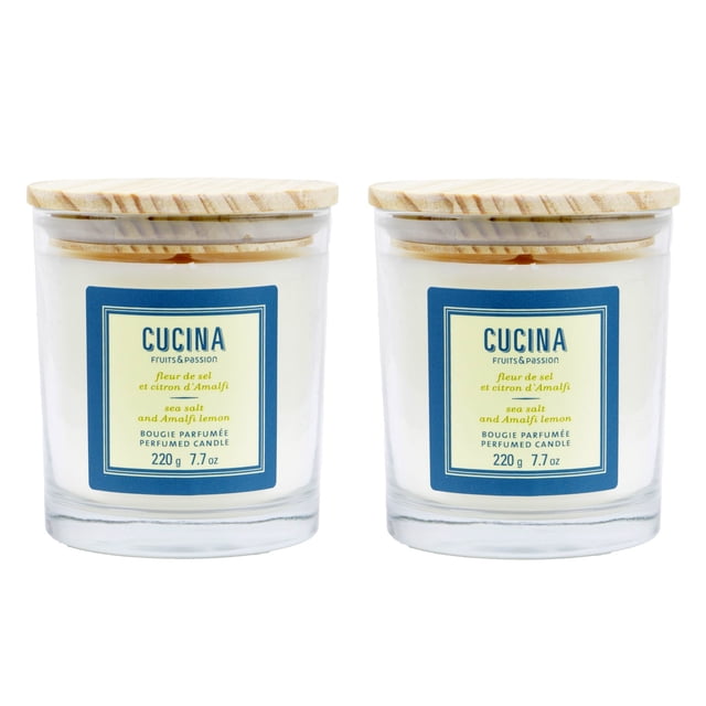 Fruits & Passion Cucina Perfumed Plant Based Wax Candle 7.7 Ounces - 2 Pack. Two handmade candles in recyclable glass jars with wooden lids, featuring a fresh Mediterranean-inspired fragrance of Amalfi lemon and sea salt. Each candle offers approximately 35 hours of burn time and is made with plant-based wax. The jars are labeled with a blue and yellow design, highlighting the eco-friendly and cruelty-free attributes of the product.