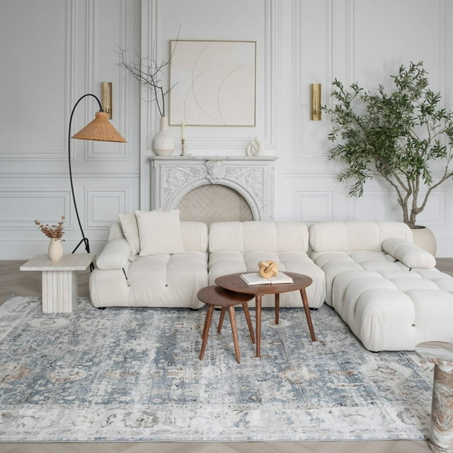 Blue distressed Rug Branch Atlas Scandinavian indoor area rug placed under a white tufted sectional sofa with wooden nesting tables in an elegant living room.