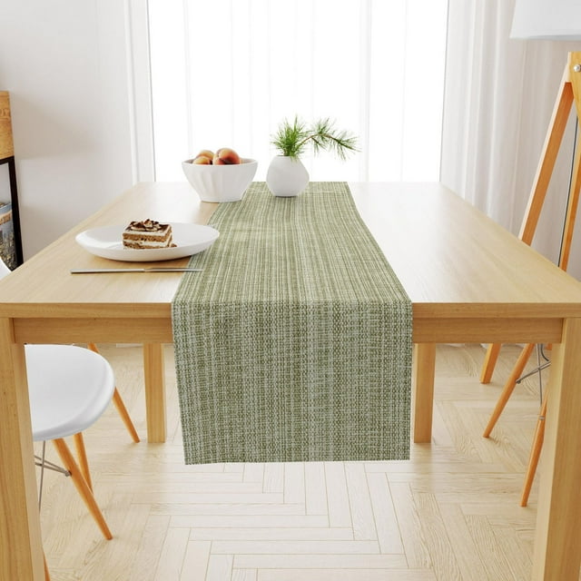 Casual classic green woven cotton table runner on a light wood dining table set with dessert plate, bowl of peaches, and small vase for kitchen or patio use.