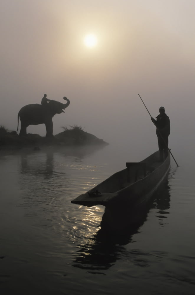 An Elephant With Its Mahout Stand At The Edge Of The Rapti River Near Sauraha And Chitwan National Park As A Man Pushes His Dugout Canoe Along The River Nepal Canvas Art - Sean White Design Pics (12