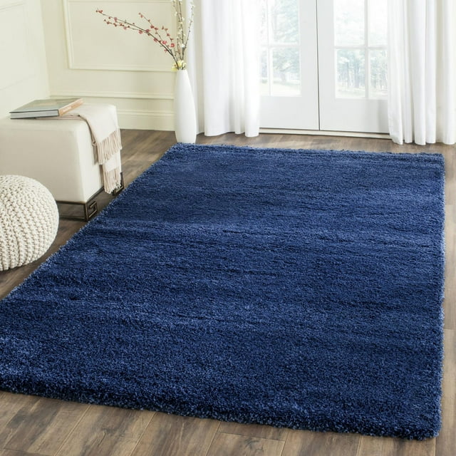 Safavieh Milan Harlow deep blue solid shag area rug displayed in a sunlit living space with wood flooring, white curtains, and minimalist decor.