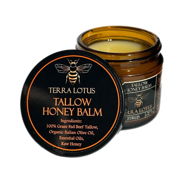 crema hidratante Terra Lotus de sebo orgánico de ternera alimentada con pasto frasco abierto, vista 3/4: tarro de vidrio ámbar con bálsamo crema claro, tapa negra en primer plano con etiqueta negra y texto naranja que muestra logo de abeja y 'TALLOW HONEY BALM' y lista de ingredientes, etiqueta lateral parcialmente visible; fondo blanco. Adecuada para hidratación corporal y uso en manos y codos secos.