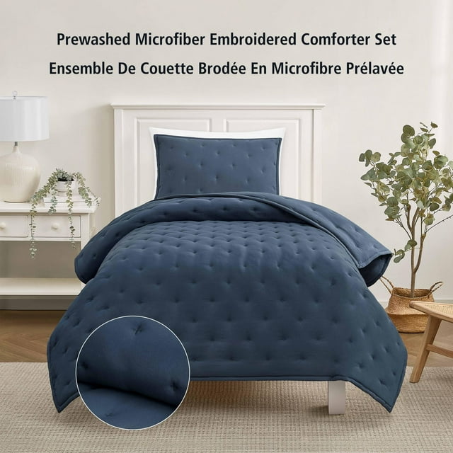 Washed indigo twin comforter and pillow sham set featuring prewashed microfiber fabric with embroidered tufted details displayed on a white bed frame in a modern bedroom.