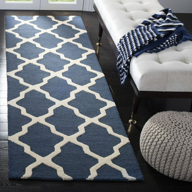 Safavieh Cambridge Liam blue runner rug with white geometric pattern on dark hardwood floor beside beige tufted bench and knitted pouf.