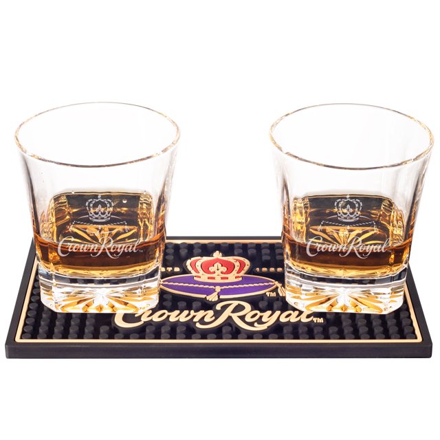 Two Crown Royal whisky glasses filled with amber liquid placed on a black mini bar mat displaying the colorful Crown Royal logo.