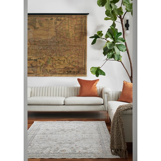 ECARPET Margaux traditional area rug with subtle floral and geometric patterns in beige and gray tones, displayed on hardwood floor between two cream sofas accented with rust-colored pillows, under vintage map wall art and near a large leafy plant.
