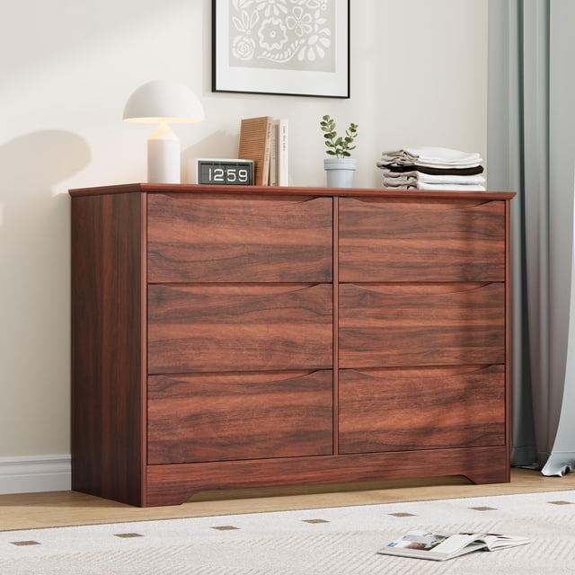 qinaqin cómoda de madera con 6 cajones, mueble alto moderno con cajones profundos y cubierta amplia color marrón; vista frontal 3/4 mostrando seis cajones con tirador oculto integrado y vetas de madera, base elevada con refuerzo interior y superficie superior usada con lámpara, reloj y ropa doblada; ideal para guardar ropa, juguetes o artículos de uso diario en recámara, sala o pasillo.