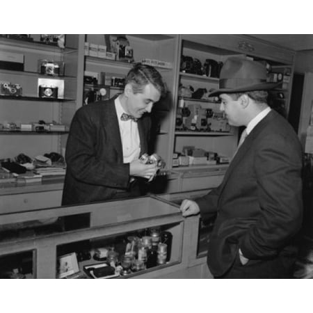 Salesman showing a camera to a customer in a store Poster Print Salesman showing a camera to a customer in a store Poster Print