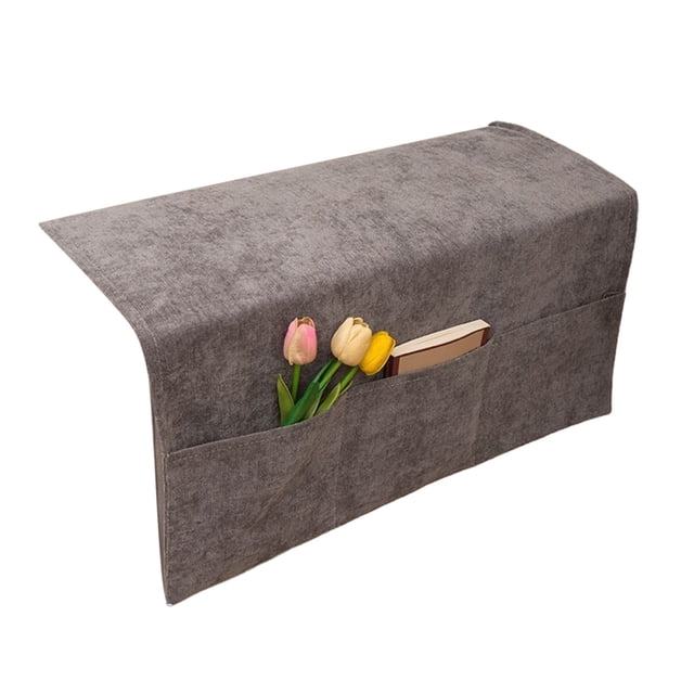 Couch arm covers in grey polyester material, designed as a non-slip slipcover for sofa armrests. Features three external pockets for storing items like TV remotes or books. The cover measures 60x110 cm (23.62x43.30 inches) and is washable, suitable for protecting armrests from wear, pet damage, and spills. Shown with flowers and a book in the pockets.