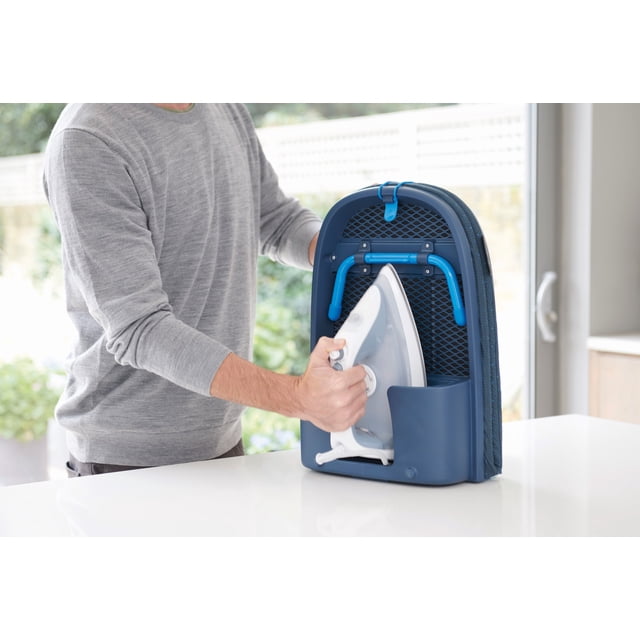 joseph joseph tabla de planchar de sobremesa plegable pocket plus - (negro y azul) tabla Pocket Plus vertical en negro y azul con patas plegables azules y soporte integrado para plancha; superficie acolchada texturizada y bolsillo rígido frontal que sostiene una plancha blanca sobre una encimera en cuarto de lavado; adecuada para planchar prendas pequeñas y retoques rápidos.