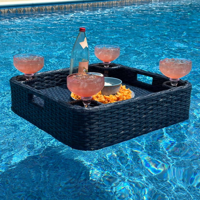 Navy wicker floating pool tray with aluminum frame holding pink cocktails, a bottle, and snacks in a clear blue swimming pool.