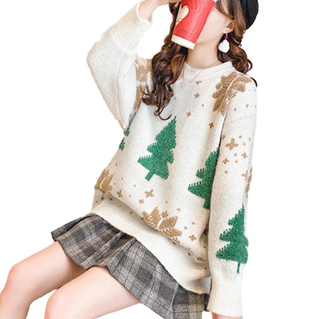 suéter de invierno para mujer, suéteres de Navidad, suéteres de punto con estampado de árbol festivo, suave, cálido, antiencogimiento, nuevo — vista 3/4 frontal de mujer sentada; suéter blanco de punto talla única con cuello redondo, dobladillo largo y suelto, árboles de Navidad verdes y copos beige en patrón tejido, mangas largas y textura suave, combinado con falda a cuadros, apropiado para otoño e invierno. A menudo usado para capas debajo de una chaqueta ligera durante salidas festivas.
