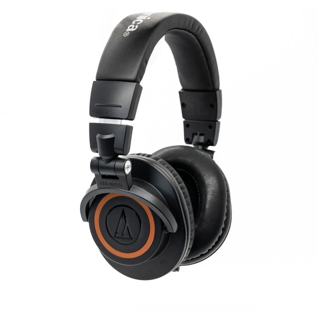 auriculares audio-technica ath-m50x professional con envoltura en bronce Vista 3/4 frontal de auriculares circumaurales Audio-Technica ATH-M50x en negro con anillo bronce en las cúpulas, diadema acolchada, copas giratorias 90° y almohadillas acolchonadas para monitoraje con un oído; también suelen usarse para revisión de mezcla en estudios domésticos. Fondo blanco.
