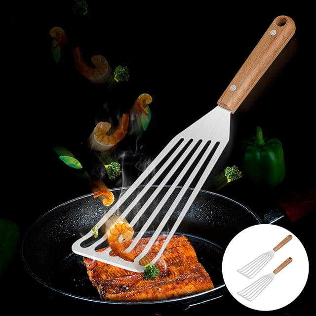 volteador de pescado perfecl acero inoxidable antiadherente mango de madera Volteador de pescado de acero inoxidable con mango de madera claro, lámina ranurada para drenar aceite, vista 3/4 que muestra la espátula levantando un filete en una sartén negra; mango con remaches y orificio para colgar, longitud total 31.CM/12.4 pulgadas. Suele usarse también para voltear filetes, tortillas o tofu.
