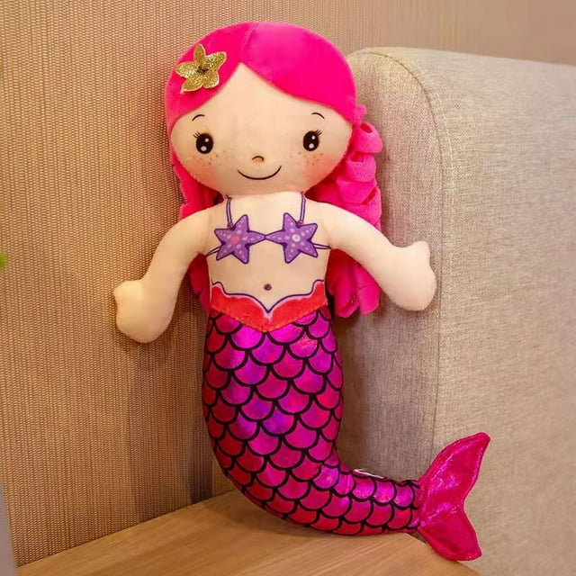 muñeca de sirena de peluche, almohada, muñeca de niña, princesa, linda muñeca, regalo de cumpleaños para niños muñeca de sirena de peluche y almohada, vista frontal centrada; cuerpo tipo cojín con cola escamada fucsia y morada, torso beige con top de conchas moradas, cabello largo rosa con adorno de estrella dorada, rostro bordado con ojos y sonrisa; apoyada en sofá claro sobre mesa de madera, adecuada como peluche, almohada o decoración infantil.