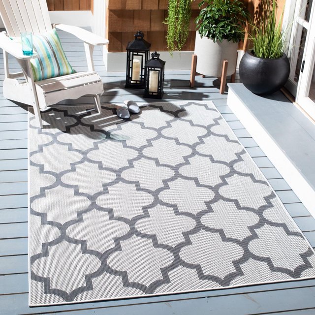 SAFAVIEH Bermuda Sophie geometric machine washable indoor/outdoor area rug in gray and white on a porch with Adirondack chair, striped pillow, black lanterns with candles, slippers and potted plants.