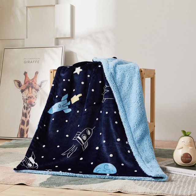 Soft reversible children's blanket with navy blue background printed with white stars and light blue rockets, paired with a plush light blue sherpa fleece backing.