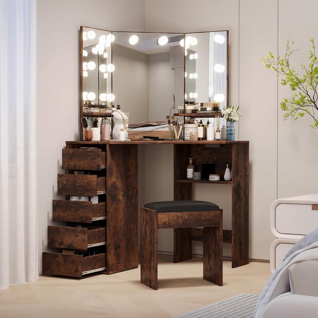 PIONEERWORKS Corner Vanity and Stool set featuring a corner vanity desk with a tri-fold mirror surrounded by adjustable lights in three color modes. The vanity includes five spacious drawers, built-in shelves, and a convenient charging station with two outlets and USB ports. Made from MDF in a rustic brown finish, the set includes a matching stool with a black cushioned seat. This vanity set for girls and women is ideal for organizing cosmetics and beauty tools in a bedroom or dressing room.