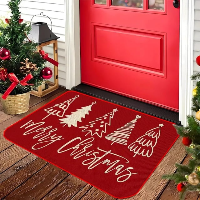 felpudo navideño con diseño de árbol de navidad rojo, ideal para interiores y exteriores, cocinas, dormitorios y baños; felpudo rectangular rojo vista 3/4 con impresión blanca de varios árboles de Navidad estilizados y texto "Merry Christmas", textura de fibra visible sobre piso de madera junto a pino y esferas, también usado como tapete decorativo en recibidores.