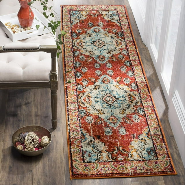 SAFAVIEH Monaco Toria traditional area rug featuring vibrant red, blue, and cream floral motifs placed on hardwood flooring beside a beige upholstered bench.