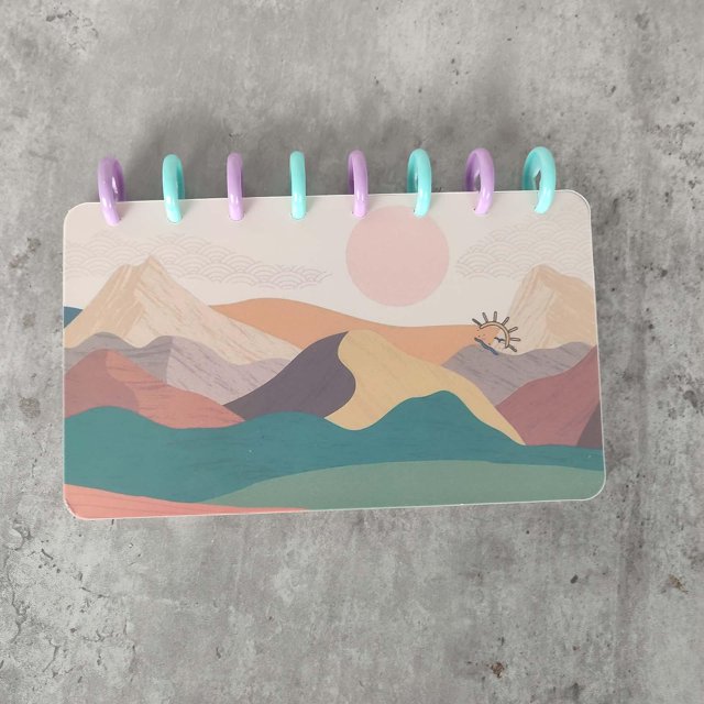 carpeta de desafío de ahorro de dinero de 52 semanas carpeta de desafío carpeta de ahorro cartera de ahorro de dinero carpeta de ahorro multicolor, vista frontal centrada de una carpeta apaisada tamaño carta (21.5 x 14.5 x 0.63 cm) con anillas plásticas turquesa y lila, cubierta ilustrada de montañas y sol en tonos pastel, papel de cartón visible, compacta y portátil sobre fondo de concreto gris. adecuada para seguimiento semanal de ahorros y uso como planificador de presupuesto.