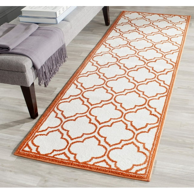 Safavieh Amherst Wilson runner rug featuring an orange geometric trellis pattern on a white background, placed on a light wood floor beside a gray upholstered bench.