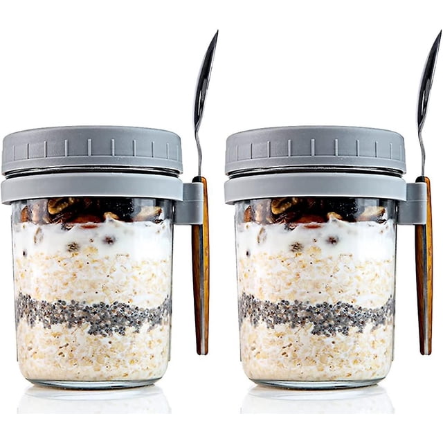 2 glass overnight oats jars with lids and spoons for milk, cereal, fruit storage mason overnight oats jars (350ml) par de tarros de vidrio de 350 ml, vista frontal; frascos tipo mason con marcas de medición visibles, tapas grises con anillo de silicón y soporte lateral que sujeta una cucharita metálica con mango efecto madera, cada tarro contiene capas de avena, semillas y yogur, fondo blanco. Ideal también como contenedor portátil para snacks o porciones individuales.