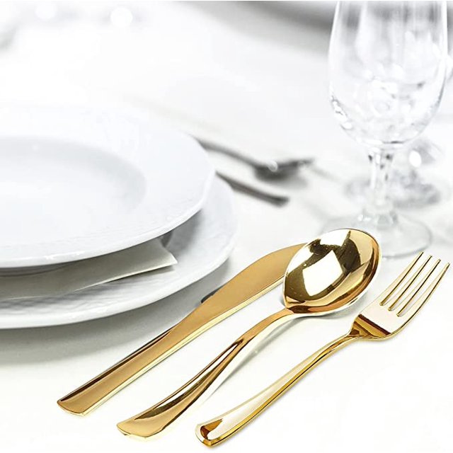 conjunto combinado de utensilios de fiesta de plástico dorado. cubiertos desechables muy resistentes. fuerte, duradero, ideal para fiestas, cumpleaños, cenas y bodas de lujo (dorado) Vista 3/4 de tenedor, cuchara y cuchillo dorados de plástico en primer plano sobre mantel blanco; acabado brillante metálico, mango recto con curva ligera y perfil robusto pensado para eventos y banquetes, platos apilados y copa desenfocados al fondo. Adecuado también para montar mesas de recepción o catering pequeño.