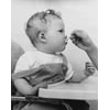 Close-up of a persons hand feeding a baby sitting in a high chair Poster Print