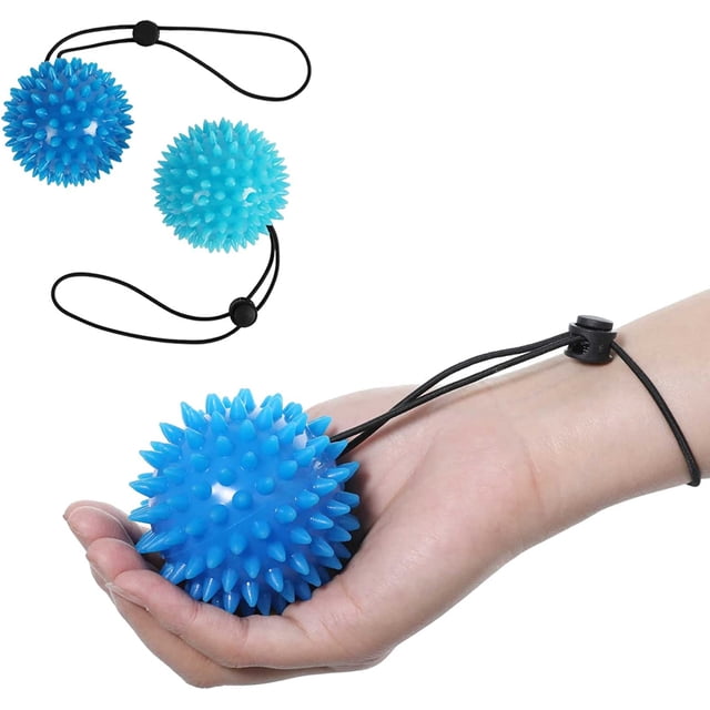 pelota de rehabilitación de manos de 2 piezas para ejercitador de manos, pelota antiestrés para adultos y niños, (2 niveles de resistencia) alivio de la ansiedad. Vista frontal de una mano sosteniendo una pelota azul con superficie de pinchos y cordón negro ajustable con tope; segunda pelota blanco‑azulada aparece desenfocada al fondo.