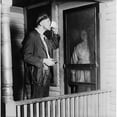 thumbnail image 2 of Homeless Man In Ragged Clothes Eating A Meal Standing As His Benefactor Keeps Her Distance Behind Her Front Door. 1919, 2 of 2