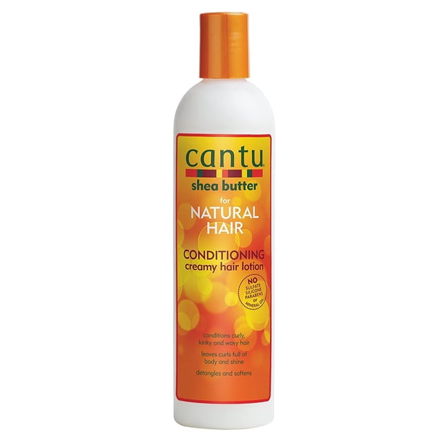 loción acondicionadora cremosa para el cabello cantu shea butter 350 ml, botella frontal blanca con tapa naranja; etiqueta amarillo‑naranja con logo Cantu y texto "for natural hair" y "conditioning creamy hair lotion", sello que indica sin sulfatos, siliconas ni parabenos; formulada con manteca de karité y aceites (coco, aguacate, oliva, mango) para desenredar y acondicionar rizos y bobinas; también adecuada para preparar rizos antes del peinado.
