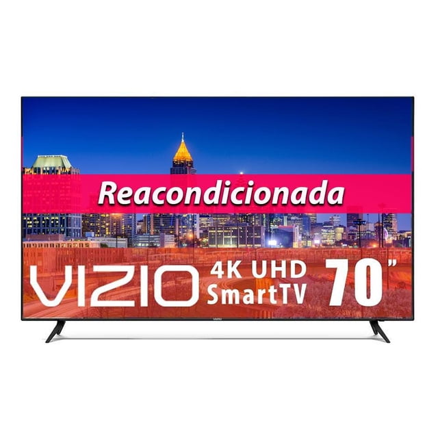 tv vizio 70 pulgadas 4k ultra hd smart tv led e70-f3 reacondicionada Reacondicionada, televisor VIZIO 70" 4K UHD con marco negro delgado en vista frontal, pantalla mostrando paisaje urbano nocturno, base de dos patas en ángulo y logotipo VIZIO en el bisel inferior. Incluye SmartCast, Chromecast y control por Google Assistant según ficha; puede presentar alteraciones estéticas o empaque genérico. Adecuada también para usar como pantalla secundaria en un estudio de edición o entretenimiento doméstico.