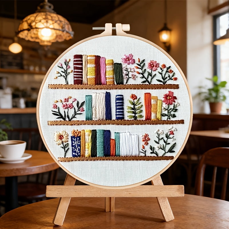 An Embroidery Kit Featuring a Bookshelf Floral Pattern Measuring, Suitable for Both Adults And Beginners. It Includes Instructions, Printed Fabric, an Embroidery Hoop, And Needle And Thread