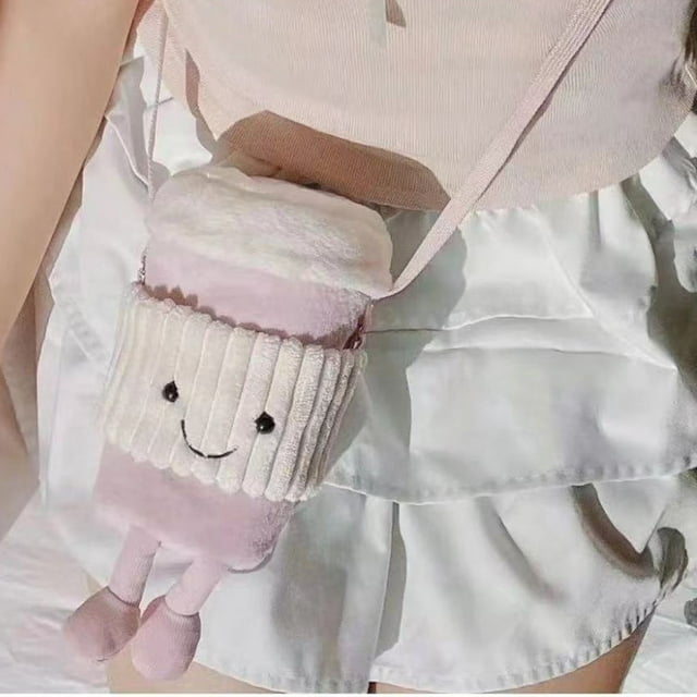 jellycat,jellycat stuffed animal, cup coffee stuffed toy endless fun -friend easter christmas birthday gifts for girls boys kids women Bolsa peluche rosa con forma de taza de café, vista frontal; manga acanalada color crema con carita bordada, tapa peluda que imita espuma, correa de hombro y piernas de peluche colgantes, mostrada sobre una persona con falda clara; adecuada como artículo para café y regalo coleccionable.