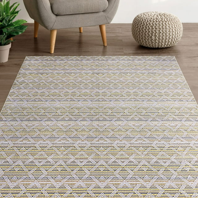 Mainstays Washable Audrey Westip Cream Printed Rug 4'x6' featuring a low-pile geometric diamond pattern in cream and muted gold microfiber, set on a wood floor near a grey armchair with wooden legs, a knitted cream pouf, and a green potted plant, suitable for living rooms, hallways, or entryways and easy to machine wash and store.