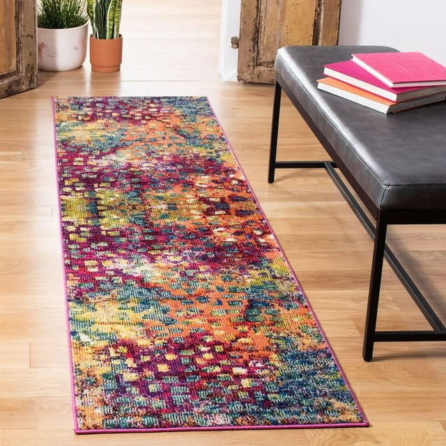 Safavieh Monaco Driskoll abstract area rug featuring vibrant multicolor pattern in pinks, oranges, yellows and blues on light wood flooring beside black bench with stacked books.
