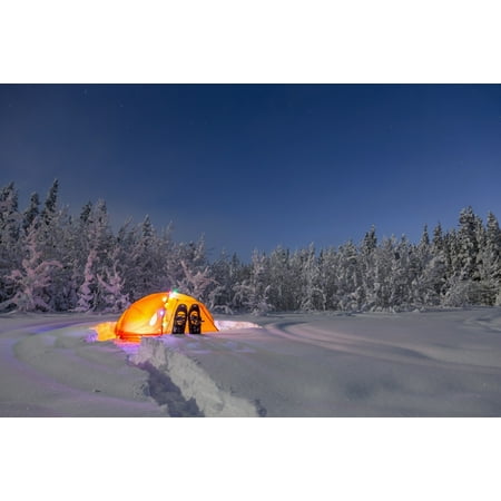 A glowing tent covered in string lights sits in the middle of an snowy spruce forest snowshoes in the deep snow outside the tent moonlight casting shadows on a clear winter night interior Alaska