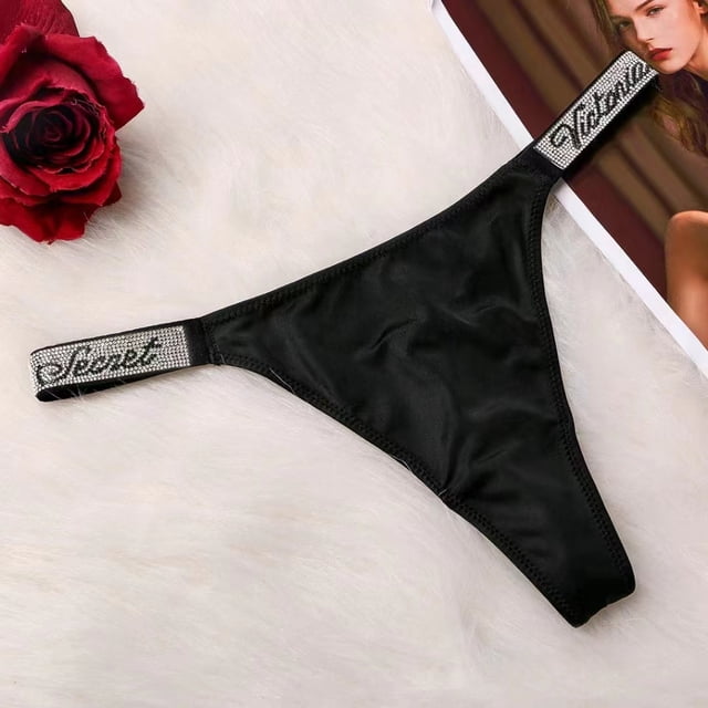 victoria secret bragas sexy sin costuras para mujer letras de lujo diamantes no . 1 tangas de imitación ropa interior diseño de marca comfort satin negro con panel frontal satinado y tiras laterales elásticas con texto 'Secret' adornadas con pedrería, vista frontal centrada sobre fondo peludo claro. A menudo usadas como pieza ligera para conjuntos de lencería.