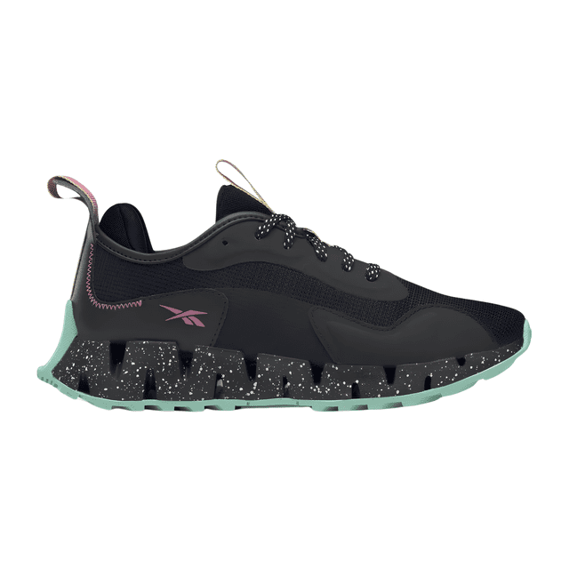 tenis reebok de mujer zig dynamica adventure hr1885 en negro, vista lateral derecha con entresuela en zigzag negra salpicada de blanco y suela exterior verde menta; parte superior de malla transpirable negra, logo Reebok lateral rosa, cordones negros, tirador trasero y refuerzo de talón; estilo urbano con influencias outdoor, ideal para ciudad y senderos.