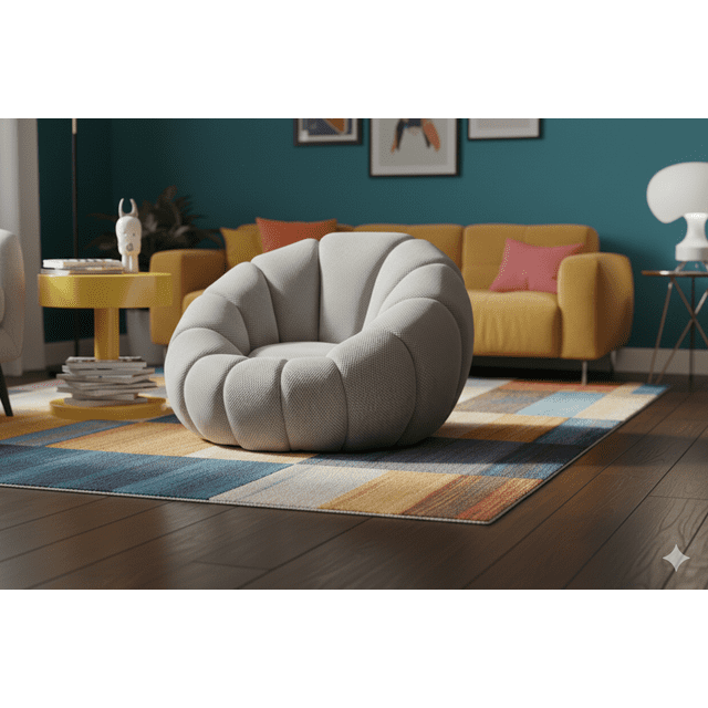 puff individual rígido tapizado moderno para sala y recámara acolchado | cómodo y decorativo EKE LIFE HOME, vista 3/4 de puff redondeado gris claro con tapizado texturizado y costuras canaladas que forman secciones acolchadas; silueta baja y estructura firme sobre alfombra frente a sofá mostaza; ideal como asiento auxiliar o elemento decorativo para sala, recámara o estudio.