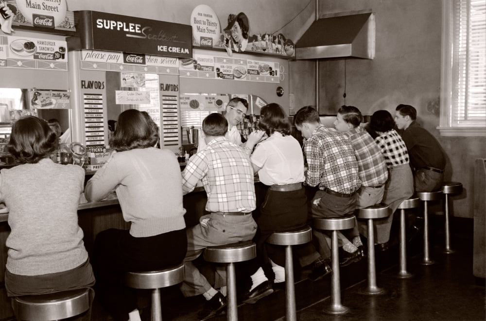 1950s Rear View Of Group Of Teenage Boys & Girls Sitting Together At A