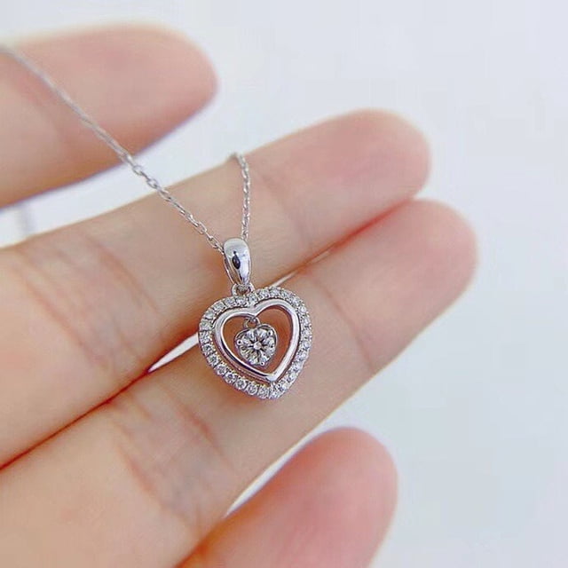 collar delicado con colgante de corazón de circonita jamw chapado en plata 1 pieza Vista frontal cercana de un collar JAMW chapado en plata con colgante doble corazón; borde exterior engastado en circonitas cúbicas y corazón interior móvil con circonita central, cadena fina tipo cable sostenida entre dedos sobre fondo neutro, suele usarse como regalo para niñas y mujeres.